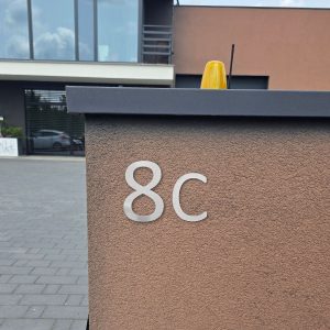 Wizualizacja przedstawiająca cyfrę i literę wykonane z aluminium. Są powieszone na bramie wjazdowej.