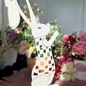 Biała dekoracja w kształcie stojącego królika na tle kolorowych kwiatów.
