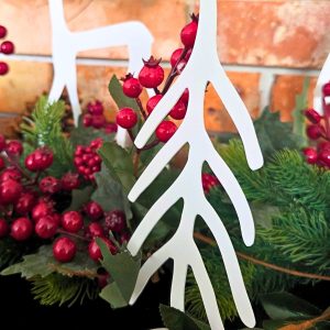 Zdjęcie przedstawia choinkę w przybliżeniu. W tle widać fragment renifera, ceglaną ścianę oraz elementy dekoracji z łańcucha iglastego oraz żurawiny.