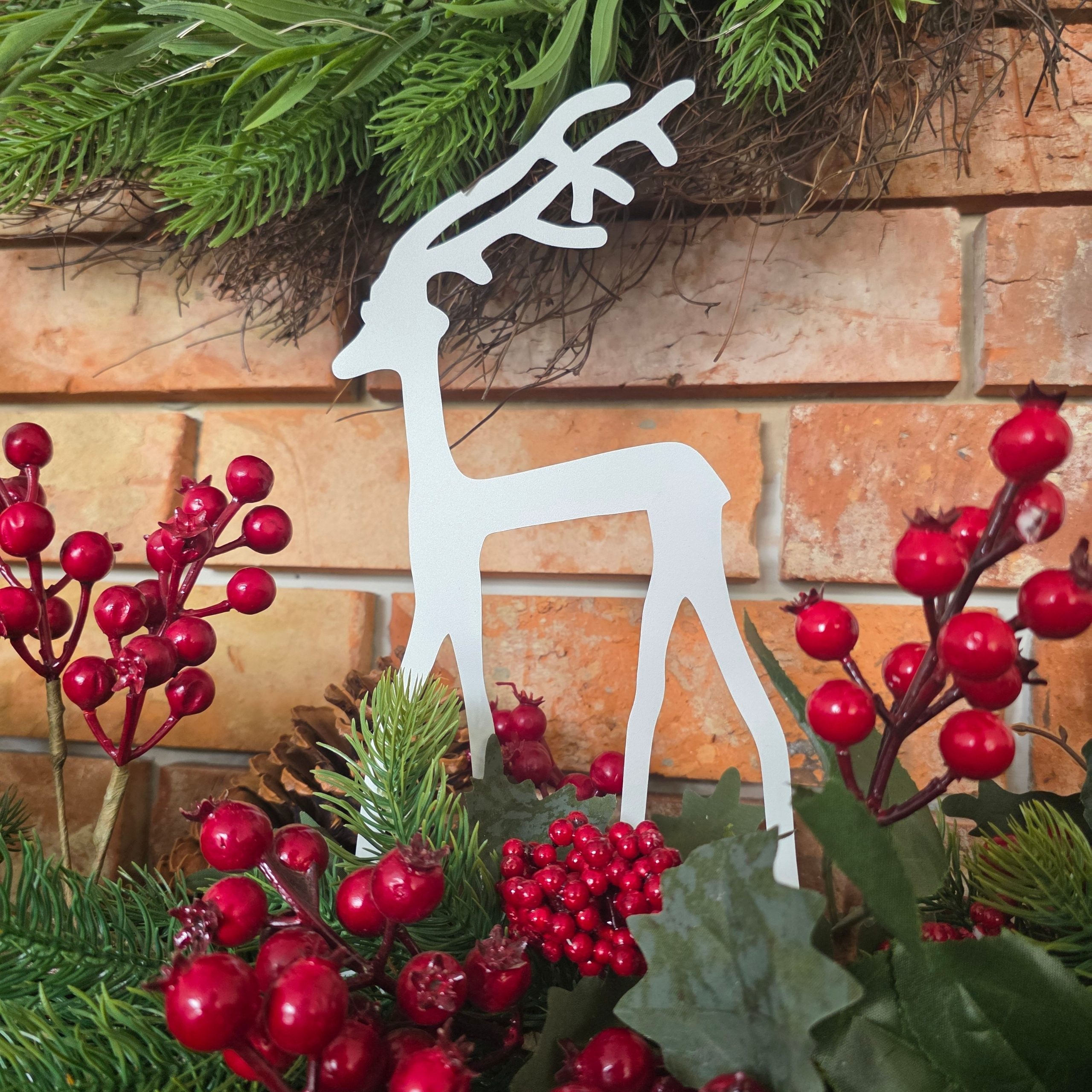 Zdjęcie przedstawia ozdobę świąteczną renifera. W tle widać jarzębinę oraz stroik świąteczny.