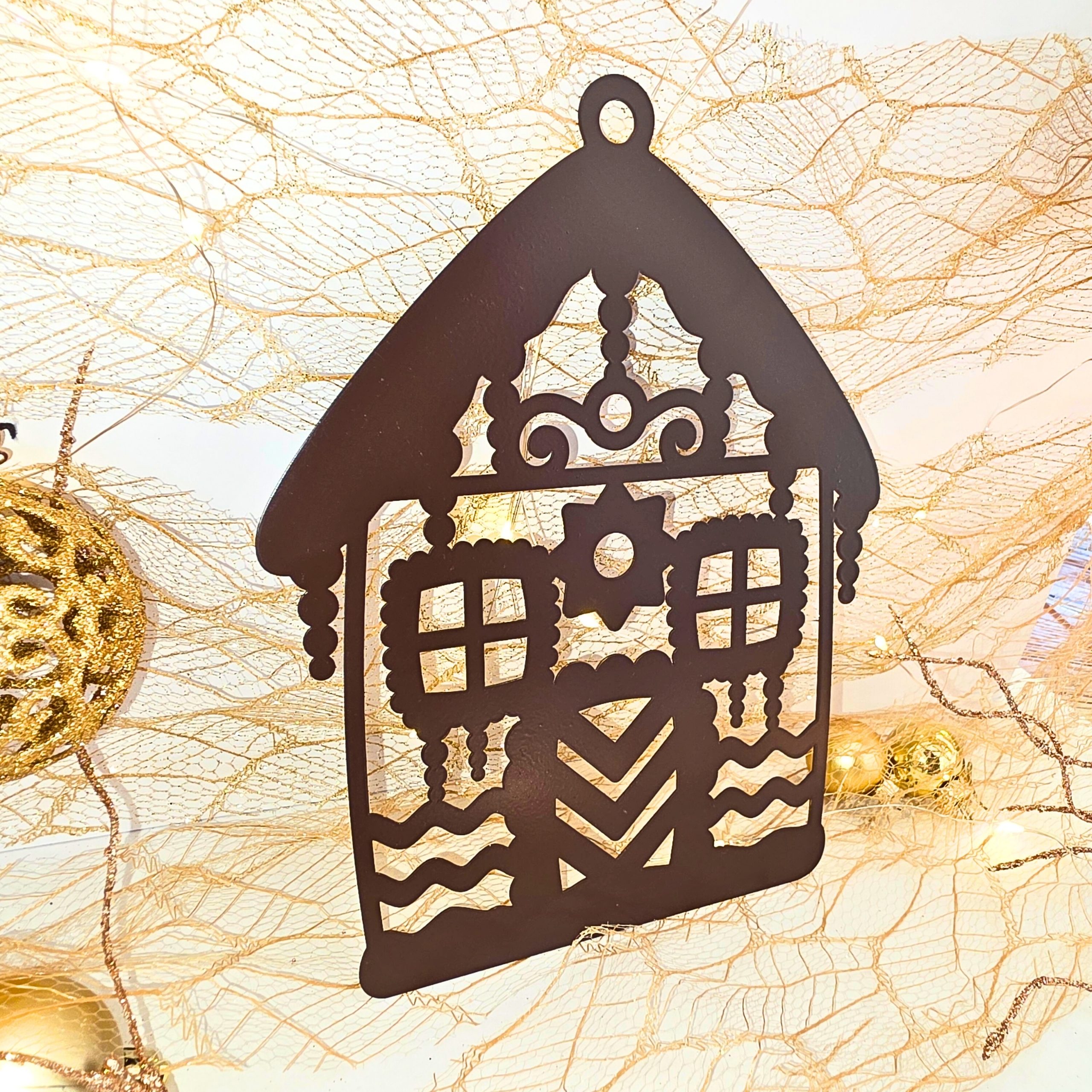 Zdjęcie przedstawia bombkę w kształcie domku z piernika. W tle widać scenkę świąteczną z bombkami, światełkami.