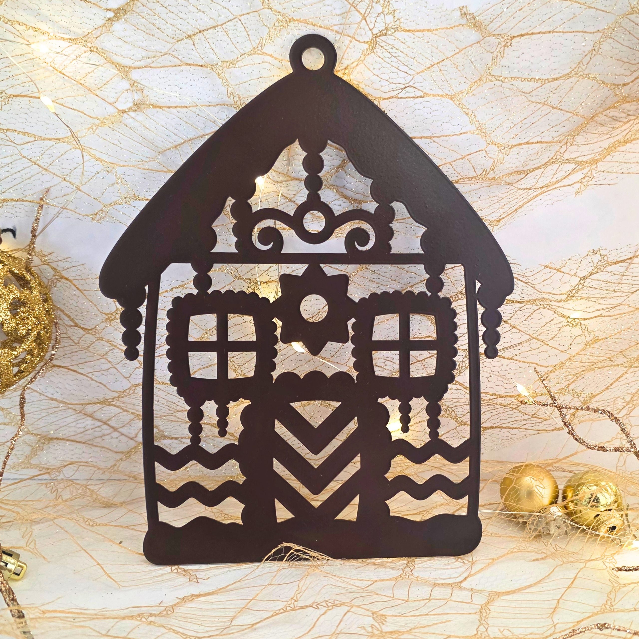 Zdjęcie przedstawia bombkę w kształcie domku z piernika. W tle widać scenkę świąteczną z bombkami, światełkami.