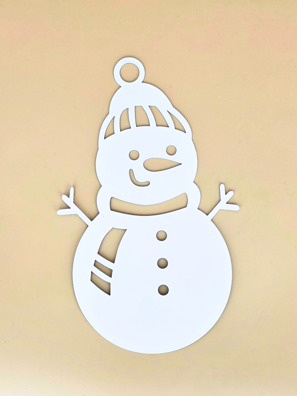 Zdjęcie przedstawia ażurową bombkę w formie białego bałwana. Bombka leży na pomarańczowym tle