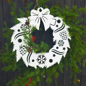 Papierowy wieniec z wyciętymi śnieżynkami i szyszkami, zawieszony wśród świeżych gałązek iglastych.