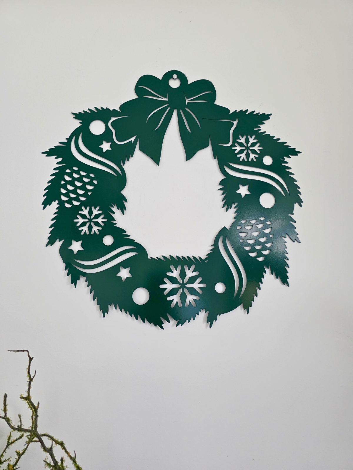 Metalowy wieniec z choinkami wiszący na białej ścianie.