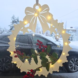 Delikatny wieniec z kokardą i lampkami LED, z zielonymi liśćmi i czerwonymi jagodami, zawieszony w oknie; w tle zimowy krajobraz i ciemny samochód.