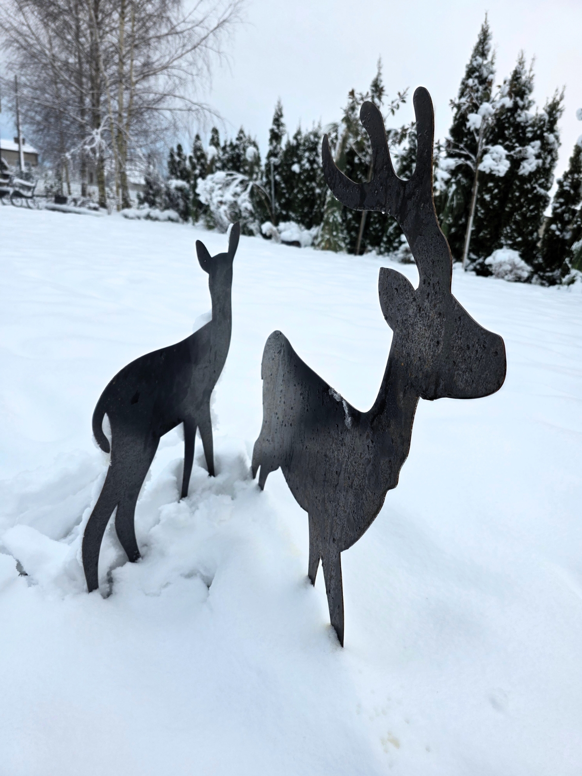 Czarna figurka jelenia z porożem i młodsza łania w zaśnieżonym krajobrazie, miękkie światło zimowego dnia.