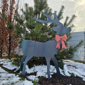 Ciemny renifer ozdobny ustawiony w śnieżnym krajobrazie obok małych drzewek.