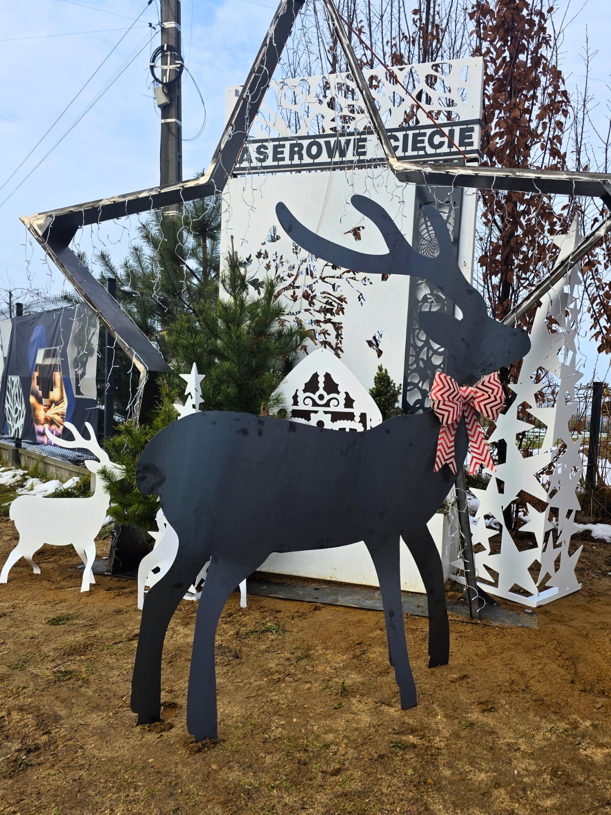 Metalowy renifer z kokardą na tle zimowej dekoracji z wyciętymi wzorami.