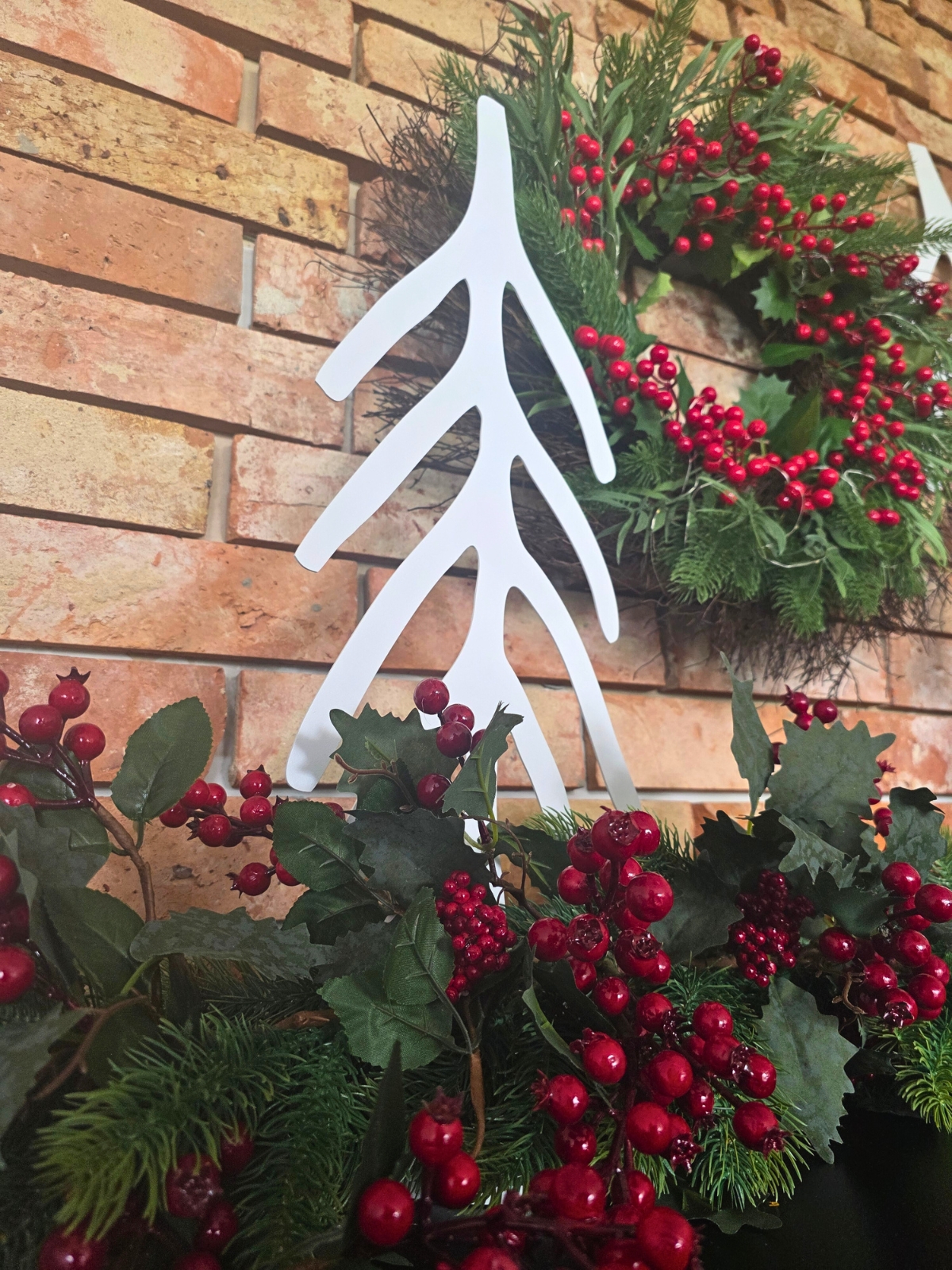 Minimalistyczna ozdoba przypominająca choinkę, ustawiona pośród świątecznych gałązek z czerwonymi owocami.