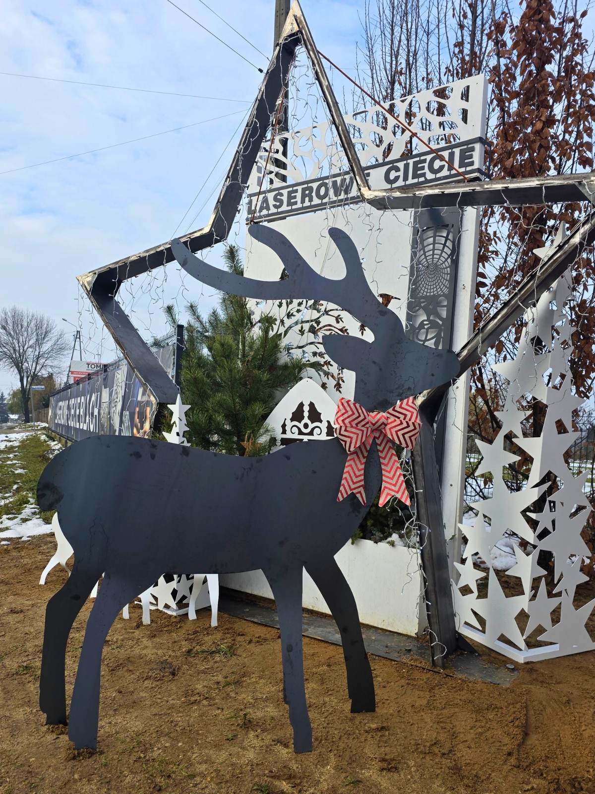 Metalowy renifer z kokardą na tle zimowej dekoracji z wyciętymi wzorami.