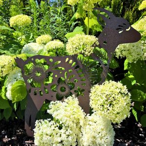 Metalowa dekoracja ogrodowa w kształcie kozy z ażurowymi kwiatowymi wzorami stojąca na tle zielonej trawy.