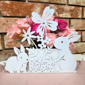 Delikatna wiosenna dekoracja z papierowymi zajączkami, kwiatami i motylem ustawiona przed ceglaną ścianą.