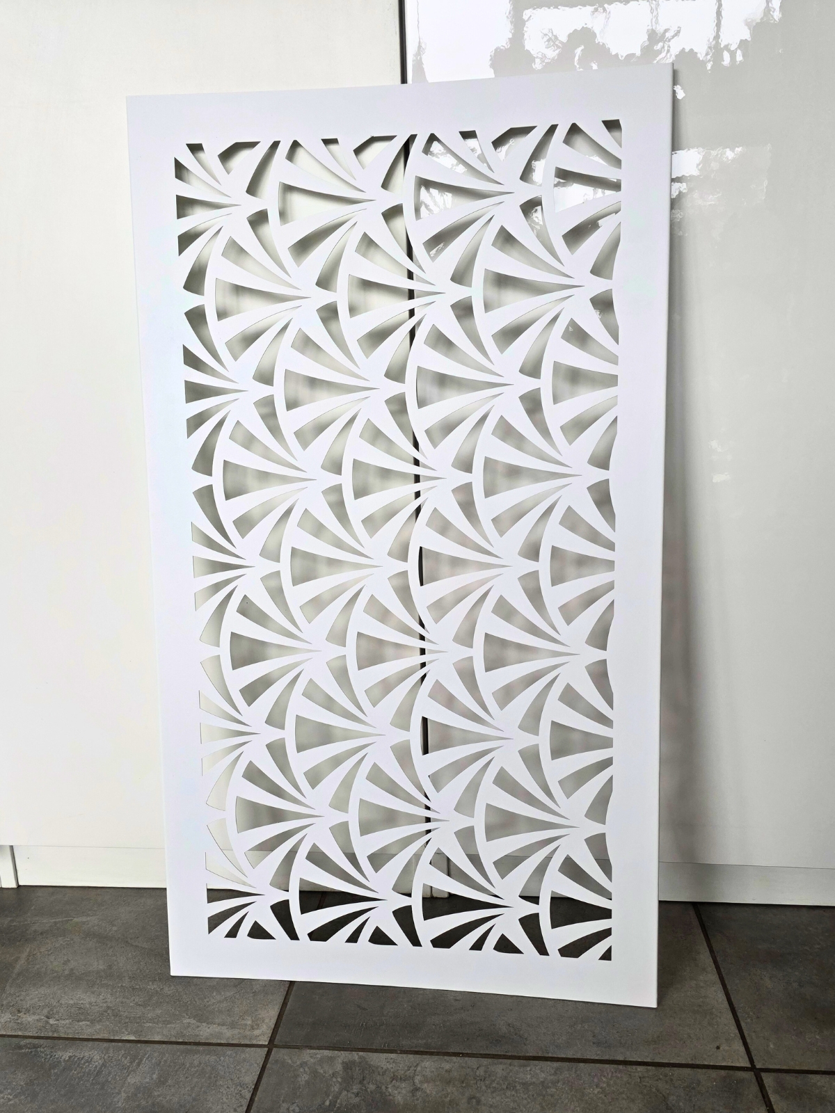 Prostokątny panel z delikatnym, geometrycznym wzorem wyciętym w białej powierzchni.