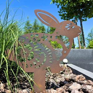 Ażurowa dekoracja ogrodowa w kształcie królika na tle roślin.