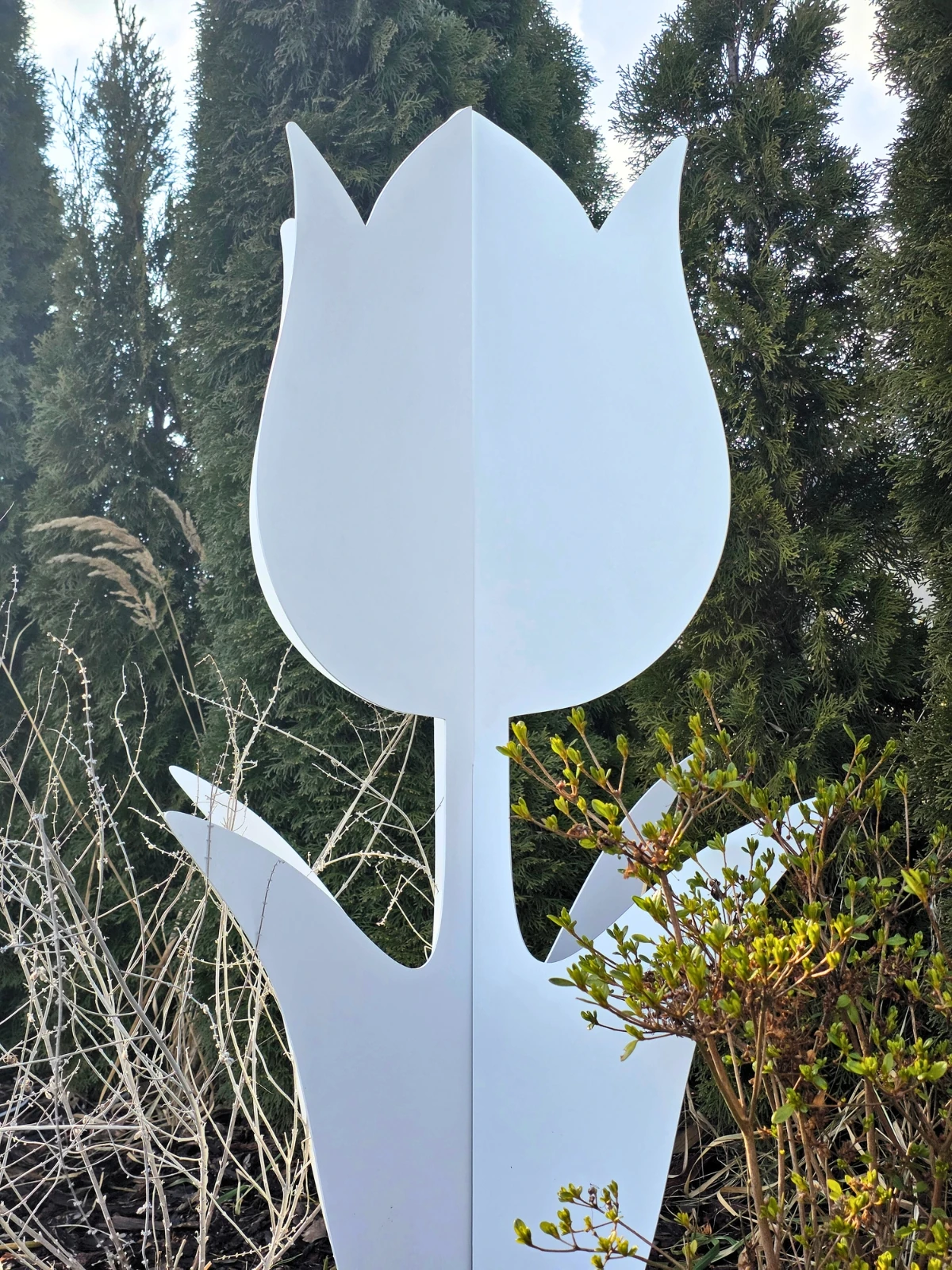 Metalowa dekoracja w kształcie tulipana stojąca wśród roślin.