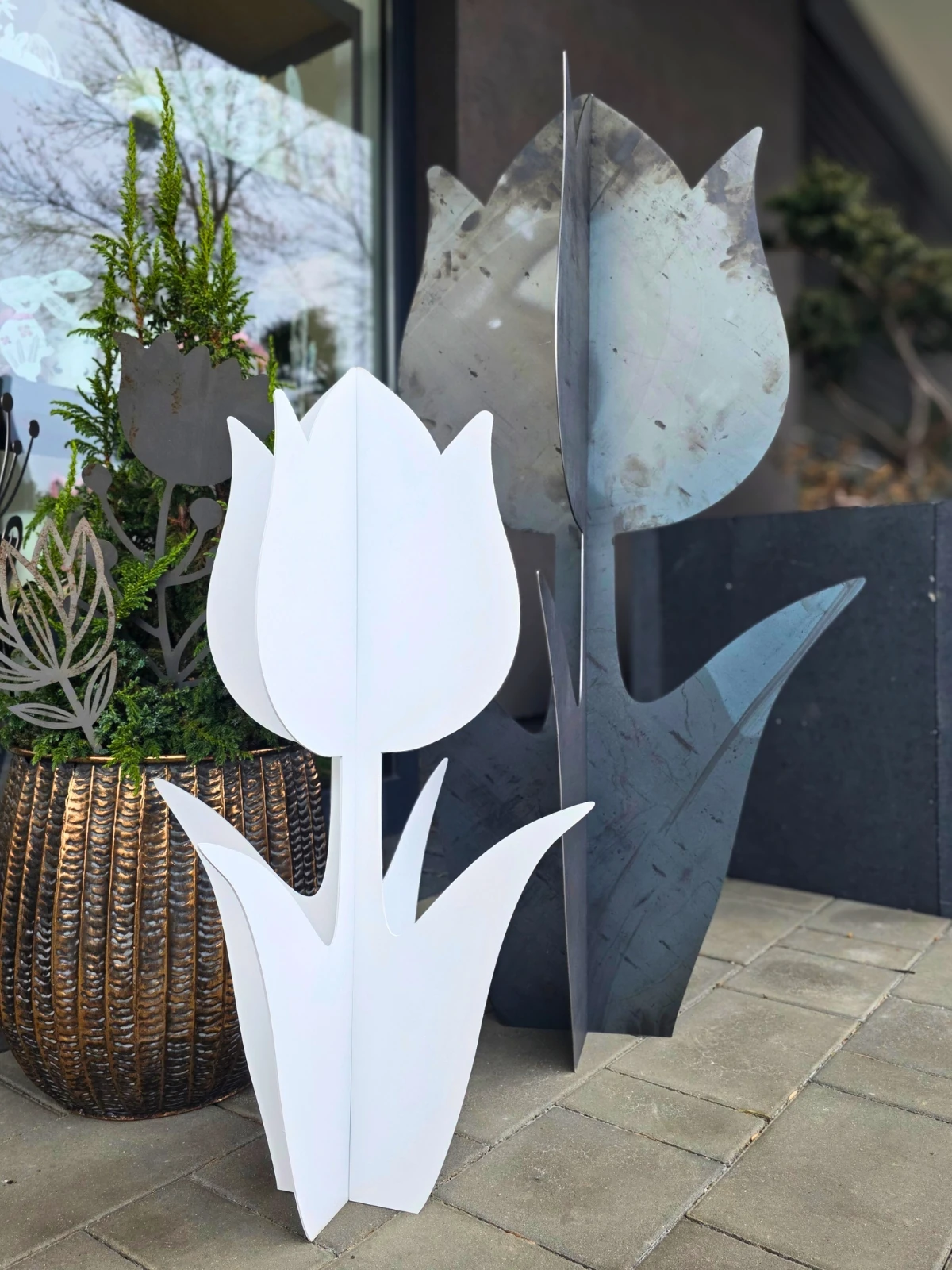 Metalowe tulipany w dwóch kolorach umieszczone przy wejściu, obok donicy z zielonymi roślinami.