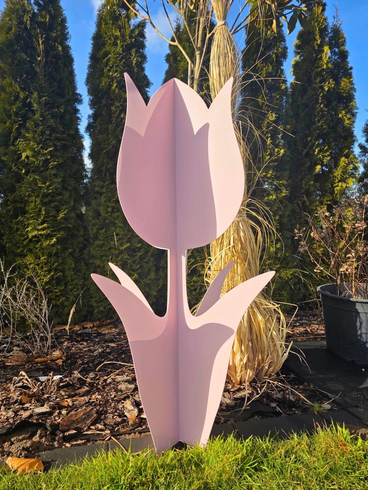 Różowa dekoracja w kształcie tulipana stojąca na trawie w ogrodzie.