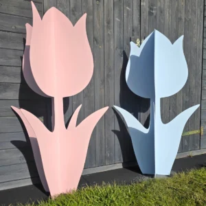 Dwie duże dekoracje w kształcie tulipanów: jedna w pastelowym różu, druga w jasnym błękicie, ustawione na tle drewnianej ściany.